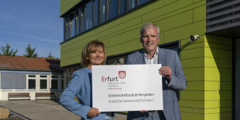 Ein Mann und eine Frau halten gemeinsam ein Schild mit Aufschrift in der Hand. 