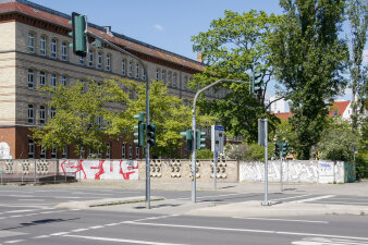 eine Ampelkreuzung an einer Straße, im Hintergrund eine mit Graffiti beschmierte Mauer