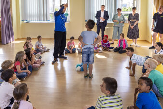 Kinder beteiligen sich an Übungen. Erwachsene schauen dabei zu. 