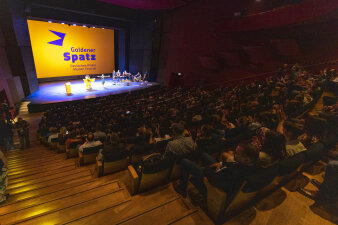 Blick durch einen Theatersaal in Richtung Bühne, auf der Leinwand steht "Goldener Spatz"