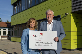 Ein Mann und eine Frau halten gemeinsam ein Schild mit Aufschrift in der Hand. 