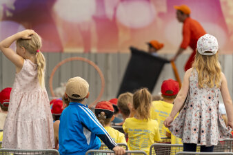 Viele Kinder sitzen vor einer Bühne. Auf der Bühne läuft ein Programm.