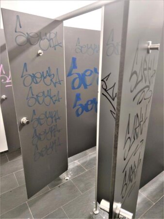 Innenraum einer öffentlichen Toilette, Wände und Türen sind mit Graffiti-Tags beschmutzt