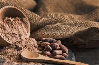 Foto: Kakaobohnen und Kakao © freepik Kakaopulver und Bohnen mit einem Holzlöffel