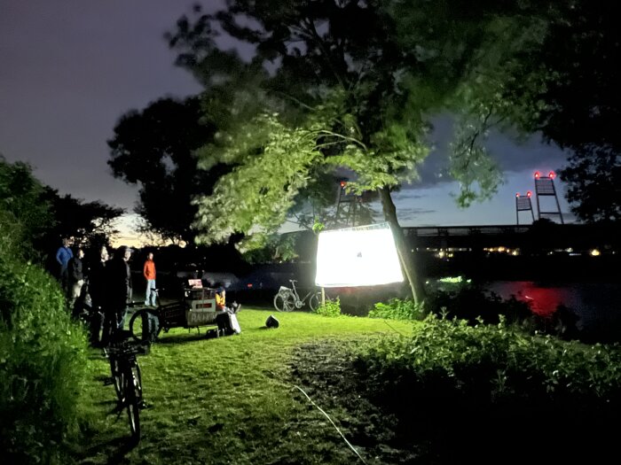 Kurzfilmradwanderung mehrere Menschen und Fahrräder befinden sich im Grünen vor einer Leinwand