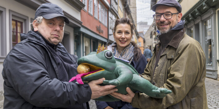 drei Personen halten einen Frosch aus Stoff in der Hand
