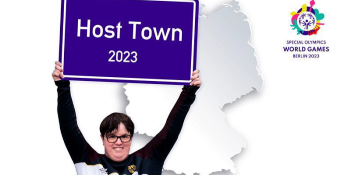 eine Frau hält ein Schild in die Höhe, auf dem "Host Town 2023" steht