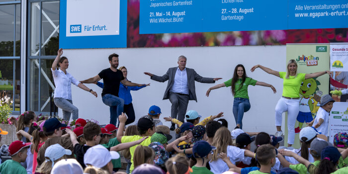 Mehrere Personen turnen auf einer Bühne. Davor stehen viele Kinder.