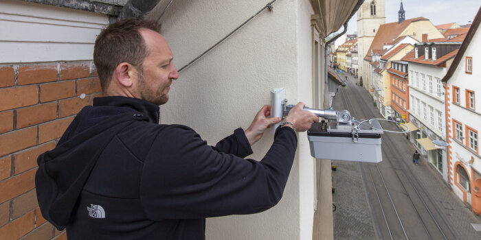 ein Mann bringt ein Gerät an einer Hauswand hoch über einer Straße an