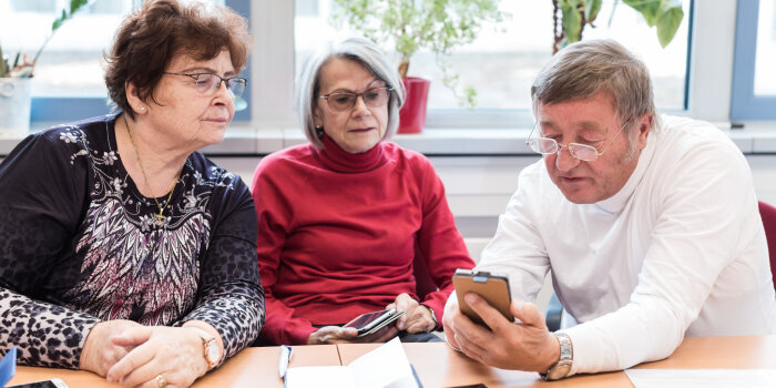 Ein Mann erklärt zwei Frauen Funktionen an einem Smartphone.