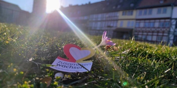 ein Zettel mit einer Herz-Grafik und dem Schriftzug "zusammen wachsen" liegt im Gras vor der Krämerbrücke