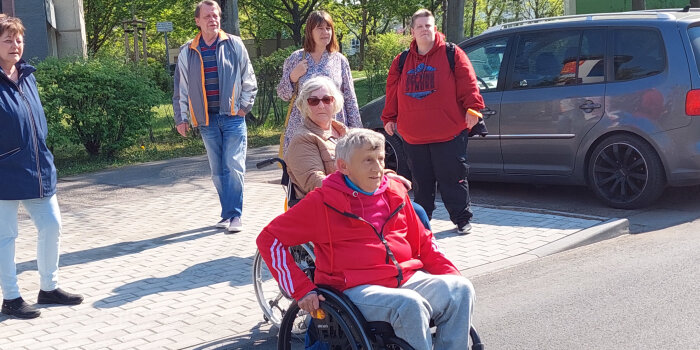 Ein Mann im Rollstuhl. Dahinter mehrere stehende Menschen.