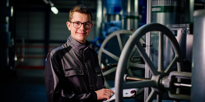 ein junger Mann in Arbeitskleidung steht an einem Maschinenrad