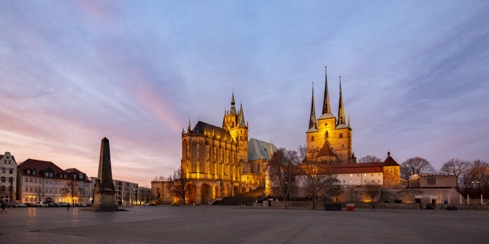 Ein großer Platz in einer Stadt. Im Hintergrund sind zwei beleuchtete Kirchen zu sehen. 