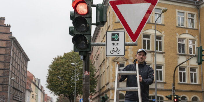 ein Mann steht auf einer Leiter neben einer roten Ampel, an der zwei Verkehrszeichen montiert sind