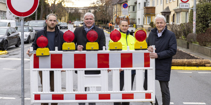 Vier Männer stehen hinter eine Verkehrsbake und heben diese an.