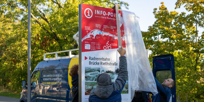 Zwei Männer stellen eine Informationstafel auf.