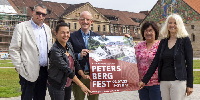 fünf Personen stehen auf einem Platz und halten ein Plakat mit dem Titel "Petersbergfest" in der Hand