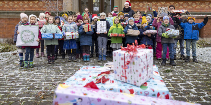 Vier erwachsene Frauen und rund 30 Kinder halten Weihnachtsgeschenke in der Hand. 