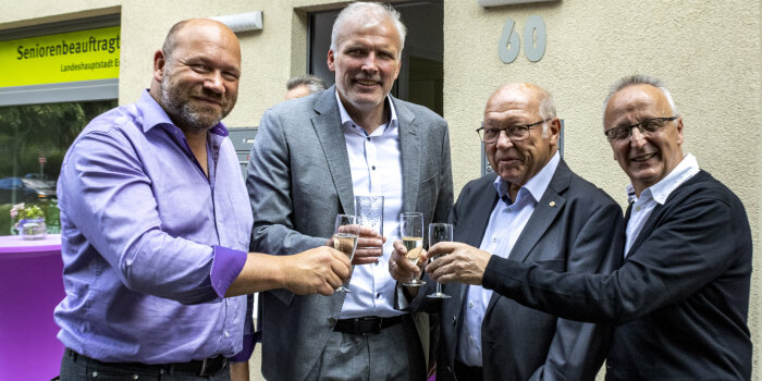 Vier Männer stehen beisammen und stoßen mit Gläsern an.