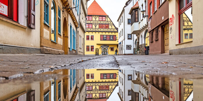 Foto: Die Große Arche © Stadtverwaltung Erfurt Eine Straße mit Fachwerkhäusern und einer großen Pfütze im Vordergrund