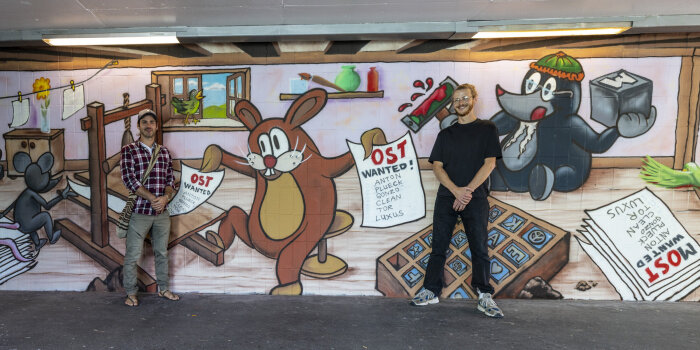 zwei Männer stehen vor einer mit Graffiti gestalteten Wand in einem Tunnel