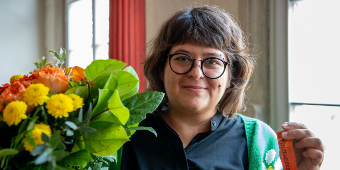 Eine junge Frau mit Brille hält einen Blumenstrauß und einen Schlüssel in der Hand