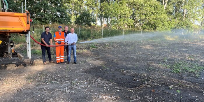 Vier Männer halten gemeinsam einen Bewässerungsschlauch an einem trockenen Waldstück.