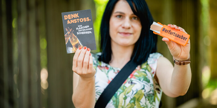 eine Frau hält eine Postkarte mit der Überschrift "Denkanstoß" und eine Pflasterbox in die Kamera