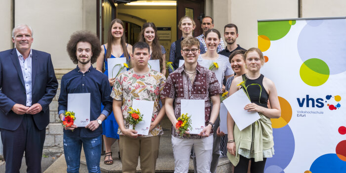 Gruppenfoto mit zwölf Menschen, von denen die meisten Zeugnisse und eine Blume in der Hand halten
