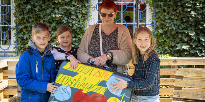 Kinder übergeben einen Koffer an eine Frau. 