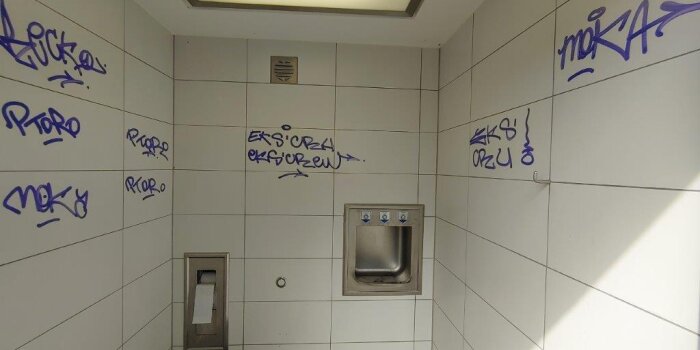 Innenraum einer öffentlichen Toilette, an den Wänden Graffiti