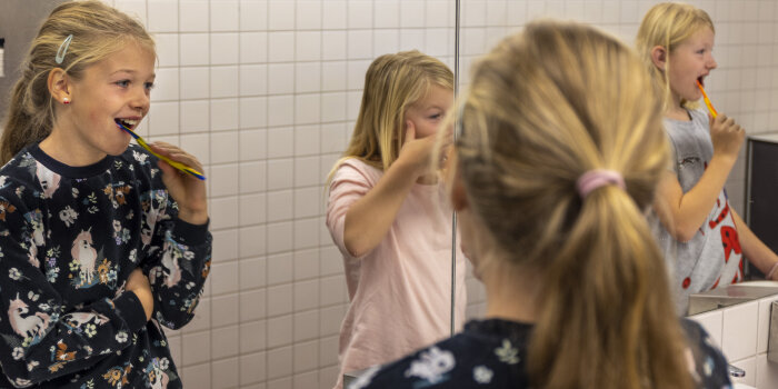 Zwei Mädchen stehen vor einem Spiegel und putzen sich die Zähne.