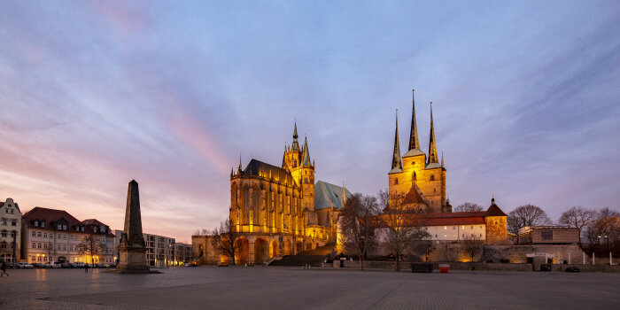 Ein großer Platz in einer Stadt. Im Hintergrund sind zwei beleuchtete Kirchen zu sehen. 