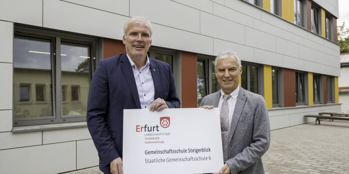 Zwei Männer halten ein Schild mit Aufschrift in der Hand. 