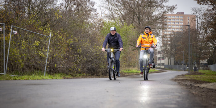 zwei Männer fahren auf dem Fahrrad eine asphaltierte Strecke entlang