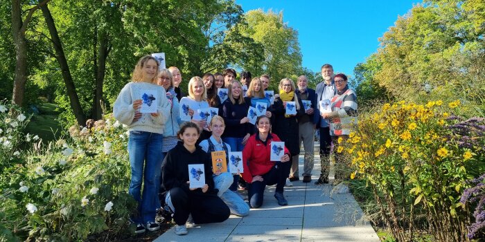 Eine gemischte Gruppe aus Jugendlichen und Erwachsenen zeigt eine Broschüre, die aus einem Schulprojekt entstanden 