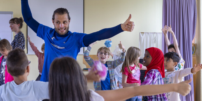 Ein Mann erklärt mehreren Kindern etwas mit Gesten.