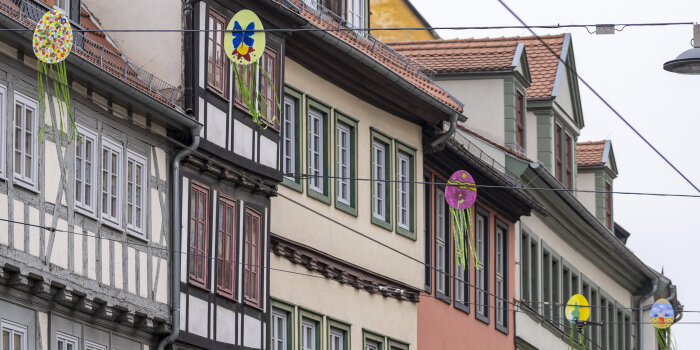 bunt bemalte Dekoration in Ei-Form hängt auf Spannseilen vor einer Häuserwand