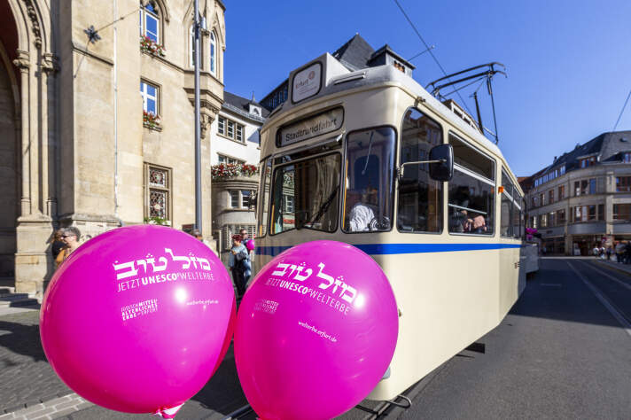 Zwei Luftballons mit der Aufschrift: Jetzt Unesco-Welterbe. Dahinter eine historische Straßenbahn. 