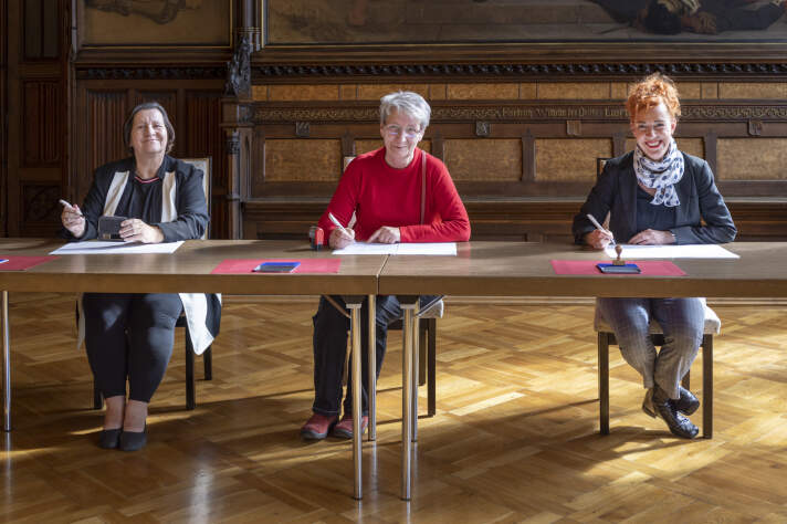 Drei Frauen sitzen an einem Tisch und unterzeichnen einen Vertrag.
