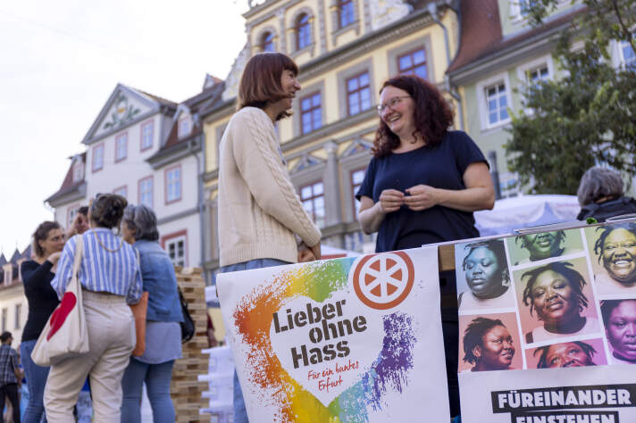 Zwei Frauen unterhalten sich an einem Marktstand. 