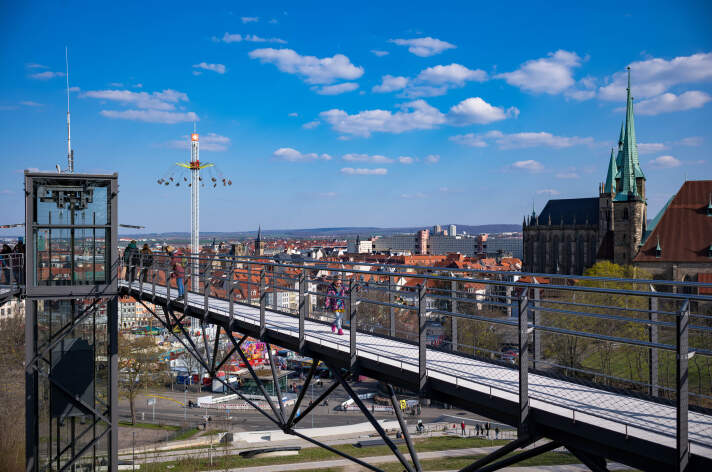 Blick auf ein hohes Kettenkarussell aus der Entfernung. Eine Brücke im Vordergrund.