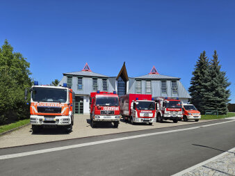 Fünf Fahrzeuge der Feuerwehr stehen in einer RReie vor einem Gerätehaus.