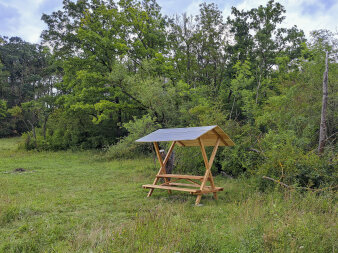 eine überdachte Holzschänke auf einer Wiese