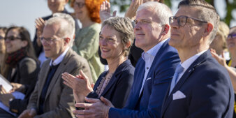 Drei Männer und eine Frau sitzen bei einer Veranstaltung nebeneinander und klatschen.