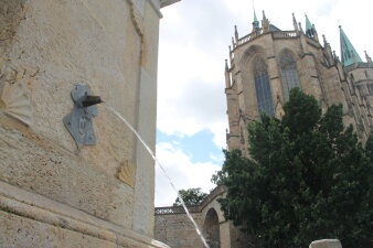 Ein steinerner Trinkbrunnen als Säule neben einem Dom.