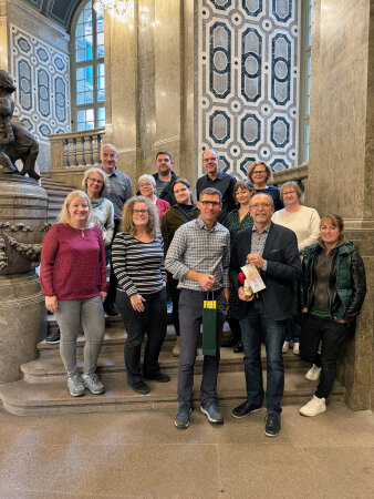 14 Menschen stehen in einem Gebäude auf einer Treppe