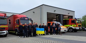 Eine Gruppe von Erwachsenen und Kindern posiert für Feuerwehrfahrzeugen mit der Flagge der Ukraine. 
