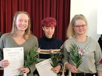 drei Personen halten Urkunden und Blumen in der Hand